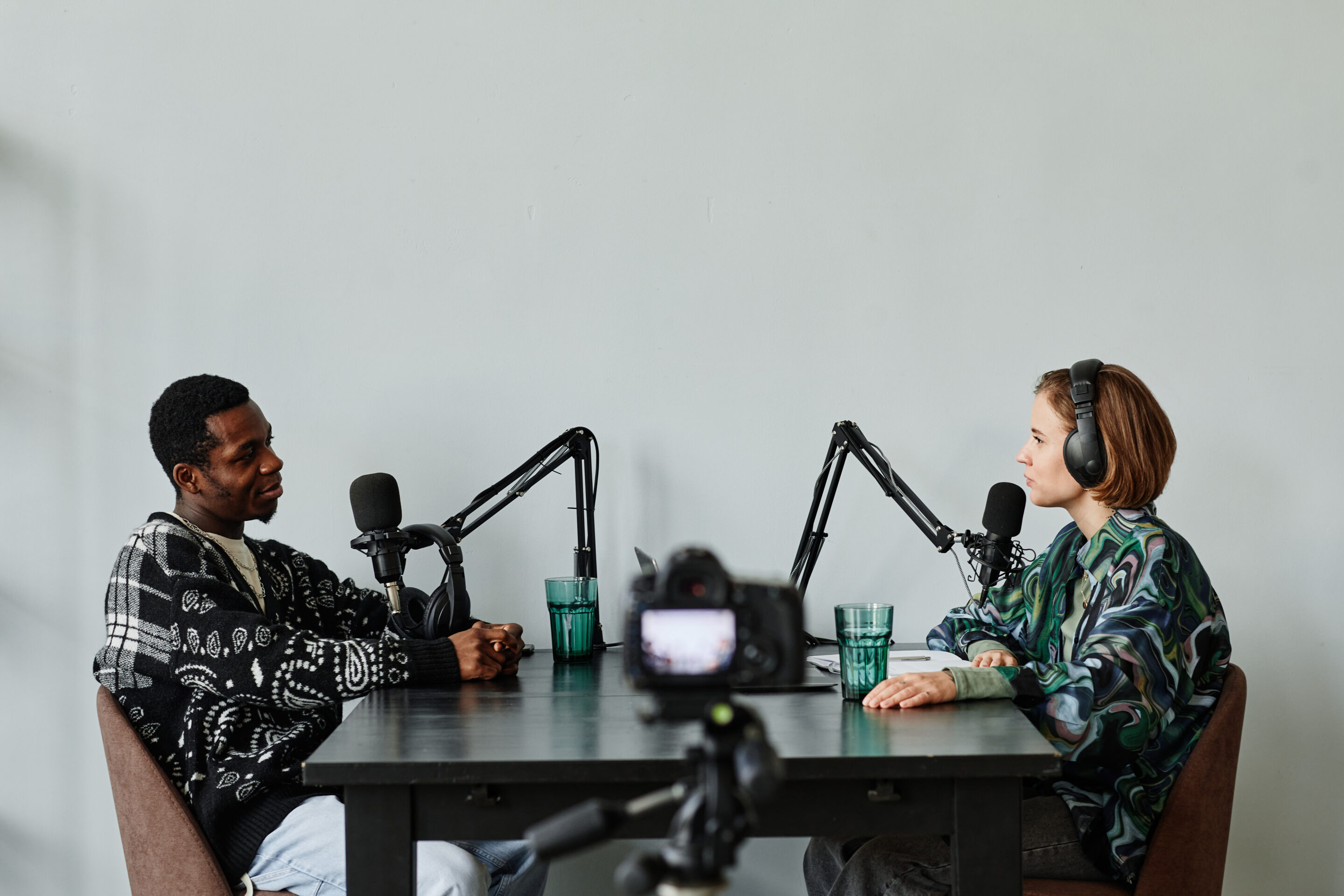 Porträt von zwei Personen, die in Mikrofone sprechen und einen Podcast im Studio aufnehmen
