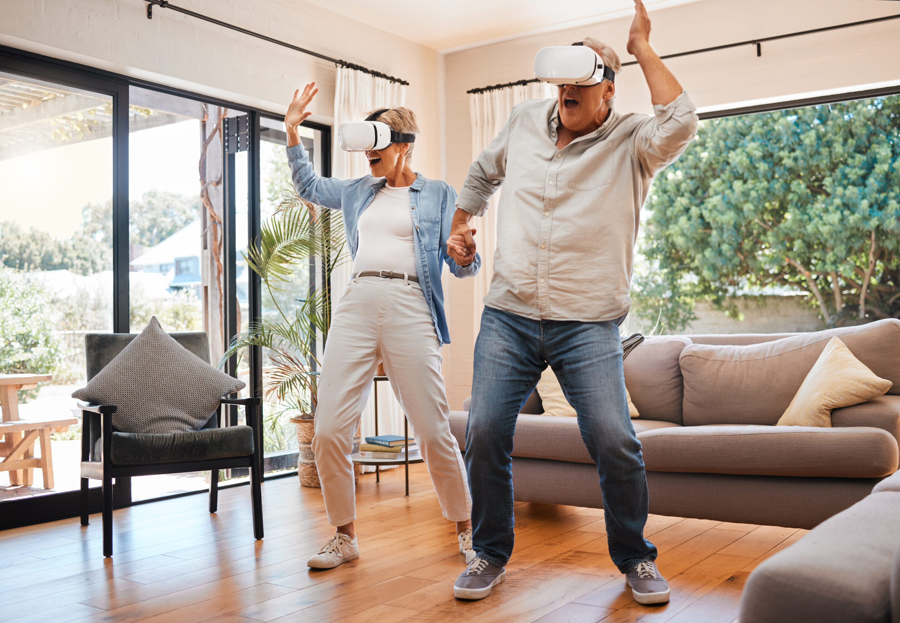 Ältere Frau und Mann tragen VR-Brillen und bewegen sich im Wohnzimmer